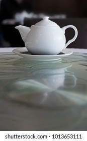 A White Teapot On A Glass Lazy Susan. 