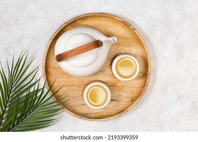 A white teapot and two cups of lemongrass tea on a wooden tray. View from above.