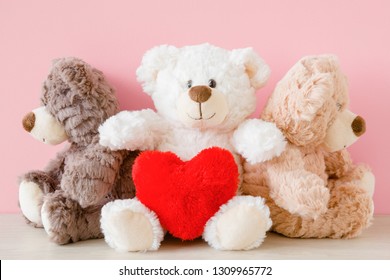 White teddy bear holding red soft heart. Sad brown bears. Two different concepts. One friend trying to make peace between two offended friends. Love triangle - choice between lovers. Front view.
