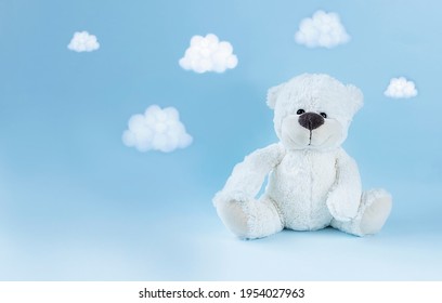White teddy bear and tiny clouds around himmon light blue background. Greeting card, baby shower invitation, baby birth, gender reveal concept. 