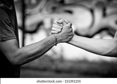 White teen and Black teen clasp hands against a wall with graffiti - Powered by Shutterstock