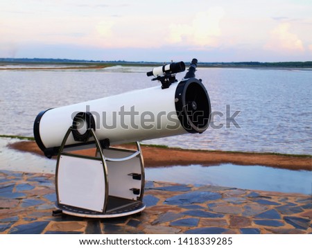 White telescope for stars Installed on a stone courtyard on the banks of a public reservoir On the background, water surface and white sky 