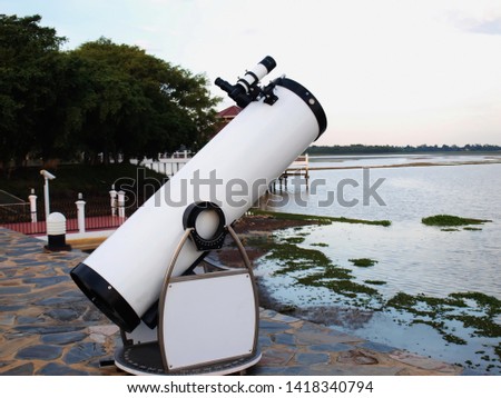 White telescope for stars Installed on a stone courtyard on the banks of a public reservoir On a green tree background and white sky 