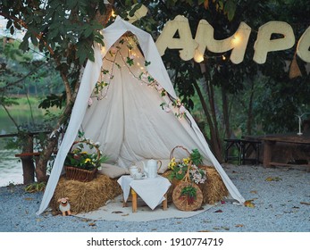 White tent with decorated light and hay seat for recreation outdoor with lake and green forest background.