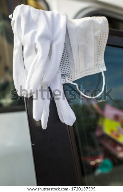 white textile mask and\
wedding gloves hanging on open car door. closeup still life, white\
car silhouette out of focus in background. Coronavirus life style\
composition