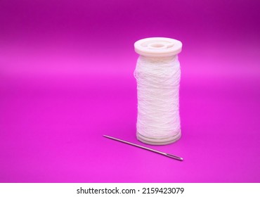 White Thread Spool With Needle Isolated On Purple Background