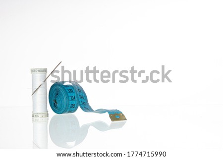 White thread in spools and cutter line for sewing and a silver needle on a white background and a measurament tape