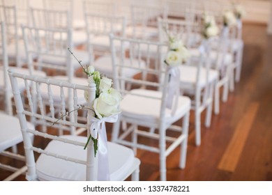 White tiffany chairs set up for ceremony with white rose posts on the end chair on aisle