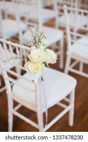 White tiffany chairs set up for ceremony with white rose posts on the end chair on aisle