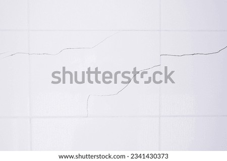 A white tiled wall with water droplets in the bathroom. Broken, cracked tiles. destroyed wall as a result of the earthquake