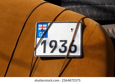 White tin plate with black number 1936, letters GE, and flag of Georgia is tied with rope to brown chair. Old license plate. Concept of transport, car repair, theft, automobile, tourism,  trip, driver - Shutterstock ID 2364872575