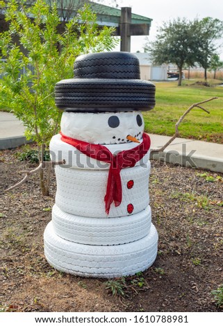 White tire snowman with a black tire hat, red scarf and stick arms.
