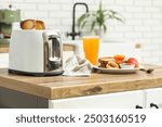 White toaster and plate with bread slices on wooden table in kitchen