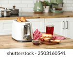 White toaster and wooden plate with bread slices on table in kitchen