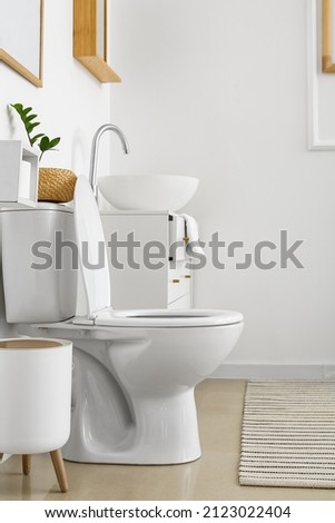 White toilet bowl and chest of drawers near light wall in restroom