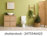 White toilet bowl, houseplant and chest of drawers with sink near green wall in restroom