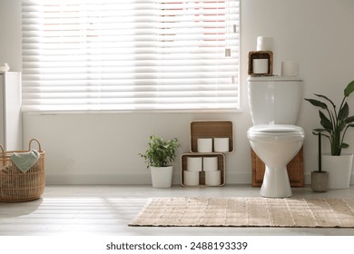 White toilet bowl, paper rolls and houseplants in bathroom