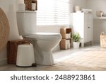 White toilet bowl, trash can and paper rolls in bathroom