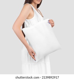 White Totebag Mockup On A Girl In A Sundress, Close-up, Isolated On Background. Texture Ecobag Template On A Dark-haired Model In A Dress, Handbag, Clothes For The Presentation Of Design, Pattern