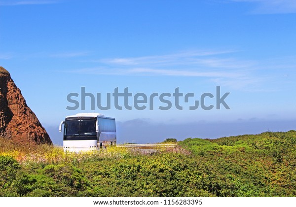 White tourist bus is driving on the\
hill, surrounded by beautiful green nature and big\
rock.