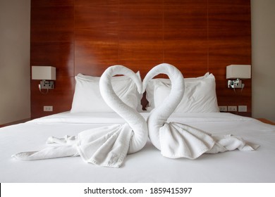 The White Towel Folded Into A Swan Shape. Placed Together In A Heart Shape On The Bed In The Bedroom.