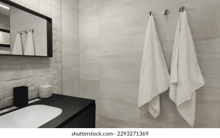 A white towel hangs on the bathroom wall, reflected in a mirror with a black and white sink. boonthavorn thailand - Powered by Shutterstock