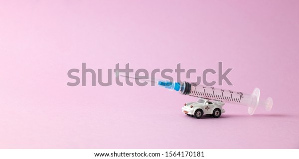 White toy car with medical syringe on pink\
background. Concept of emergency medical aid and health care.\
Banner design, space for\
text
