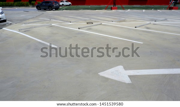 White traffic arrow\
sign with white lines and  concrete wheel stoppers in parking lot\
or outdoor car park area
