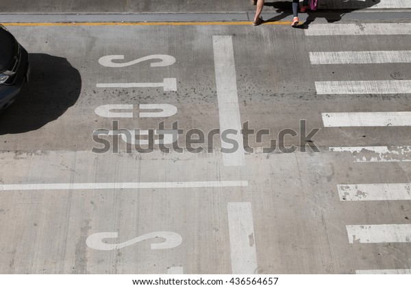 white traffic STOP sign on\
concrete street road caution black car driver in front of zebra\
crossing, legs of two pedestrian people are crossing at\
crosswalk.
