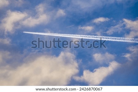 White trail of plane flying among white clouds in blue sky