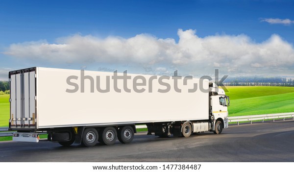 White trailer on the\
highway, against the background of a green field. There is a place\
for advertising
