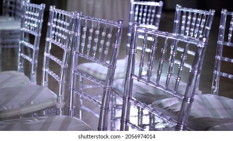 White Transparent Plastic Chiavari Chairs In Rows. Indoor Wedding Ceremony, Event, Seminar Or Party, Stage Blue Light. Concert Hall With No People.