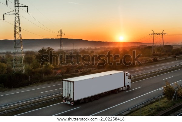 White Transportation truck along the highway\
in dreamy sunset. Highway transportation with setting sun and hazy\
sun rays in the\
background