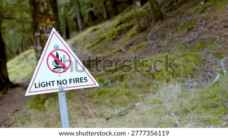 A white triangular sign prohibits lighting fires along a lush, moss-covered woodland hiking trail.