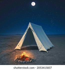 White, triangular-shaped camping tent under the starry sky and the moon. Tent and campfire. Fire to make something to eat and warm up 