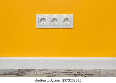 White triple outlet installed on the yellow wall, front view.