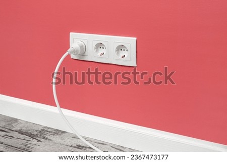 White triple outlet installed on pink wall with inserted white electrical plug, side view.