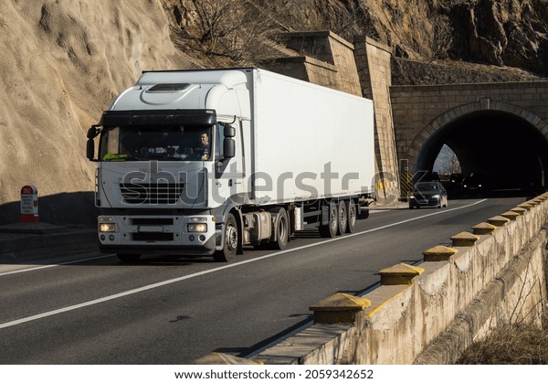 White truck carrying\
freight or goods on the highway, at the exit of a tunnel. This is a\
Iveco truck. Cargo transportation concept. Severin, Romania,\
October 13, 2021
