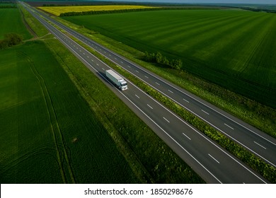 white truck driving on asphalt road along the green fields. seen from the air. Aerial view landscape. drone photography.  cargo delivery . cargo delivery and transportation concept