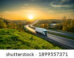 White truck driving on the highway winding through forested landscape in autumn colors at sunset