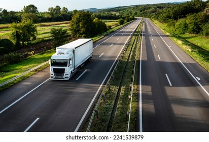 White truck driving on the highway winding through forested landscape in autumn colors at sunset