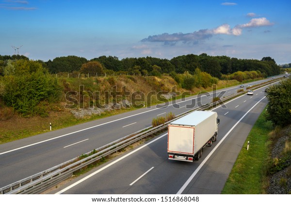 white truck is driving on the highway through the\
country landscape under a blue sky with clouds, transport and\
environment concept, copy\
space