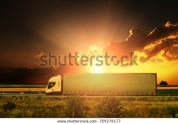 White truck with the grey trailer on the\
countryside road against night sky with\
sunset