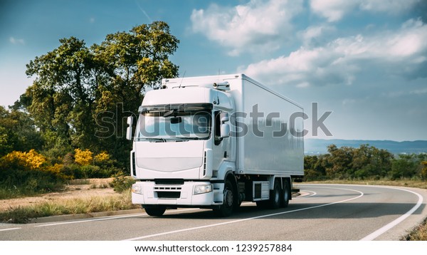 White Truck Or\
Traction Unit In Motion On Road, Freeway. Asphalt Motorway Highway\
Against Background Of Mountains Landscape. Business Transportation\
And Trucking Industry