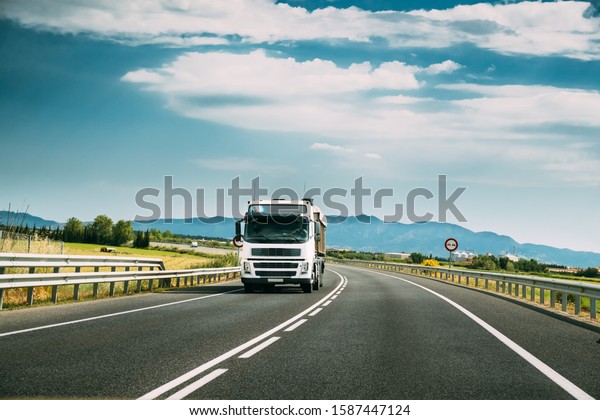 White Truck Or\
Traction Unit In Motion On Road, Freeway. Asphalt Motorway Highway\
Against Background Of Mountains Landscape. Business Transportation\
And Trucking Industry.