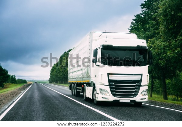 White Truck Or Tractor Unit, Prime Mover,\
Traction Unit In Motion On Road, Freeway. Asphalt Motorway Highway\
Against Background Of Forest Landscape. Business Transportation And\
Trucking Industry