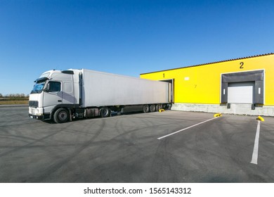 white truck with a white trailer at unloading at the warehouse.Warehouse complex with an asphalt pad and truck with blue sky