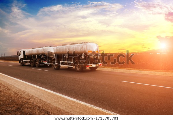 White truck witha trailer\
shipping milk on a countryside road against a night sky with a\
sunset