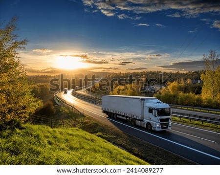 White trucks driving on the highway winding through forested landscape in autumn colors at sunset