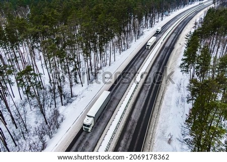 white trucks on the higthway. convoy  whith cargo driving by road seen from the air. Top view landscape. shooting from a drone. Cargo delivery in winter. Aerial view of snow road in winter forest 